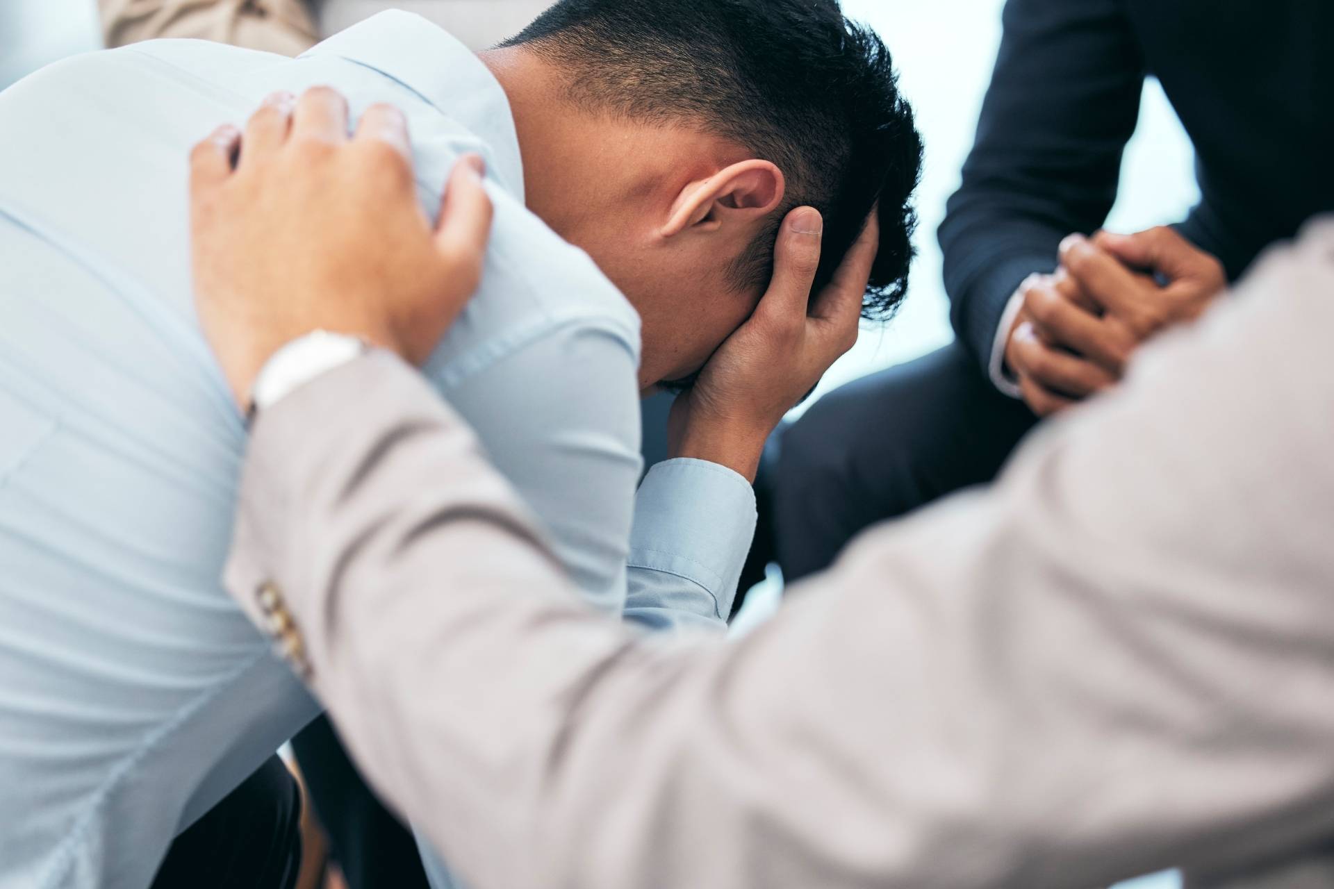 Depressed man sitting while supportive peers offer comfort and encouragement in a wellness center setting